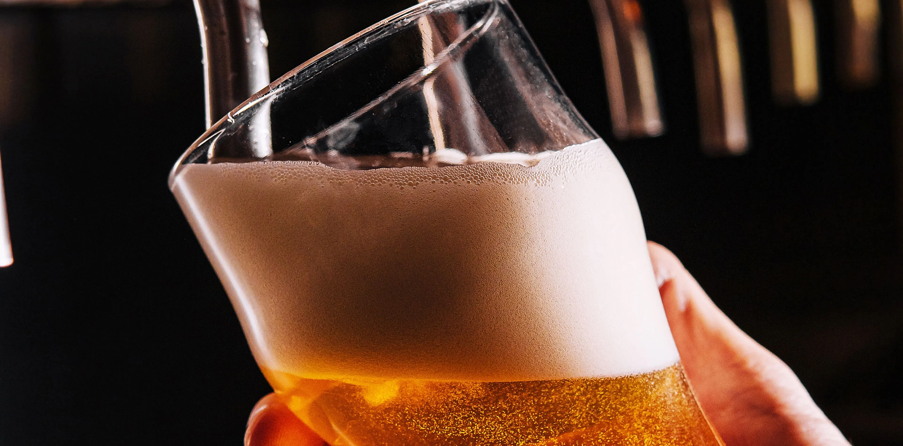 Verre incliné rempli de bière dorée avec une mousse épaisse, servi d’une tireuse à bière.