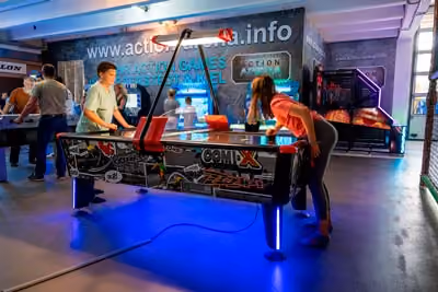Junge und Mädchen spielen Air-Hockey in einer farbenfrohen Spielhalle mit neonbeleuchteten Tischen.