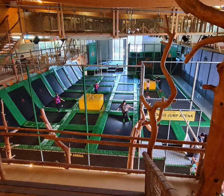 Inneneinrichtung eines Trampolinparks mit Kindern, die auf grünen Trampolinen springen.