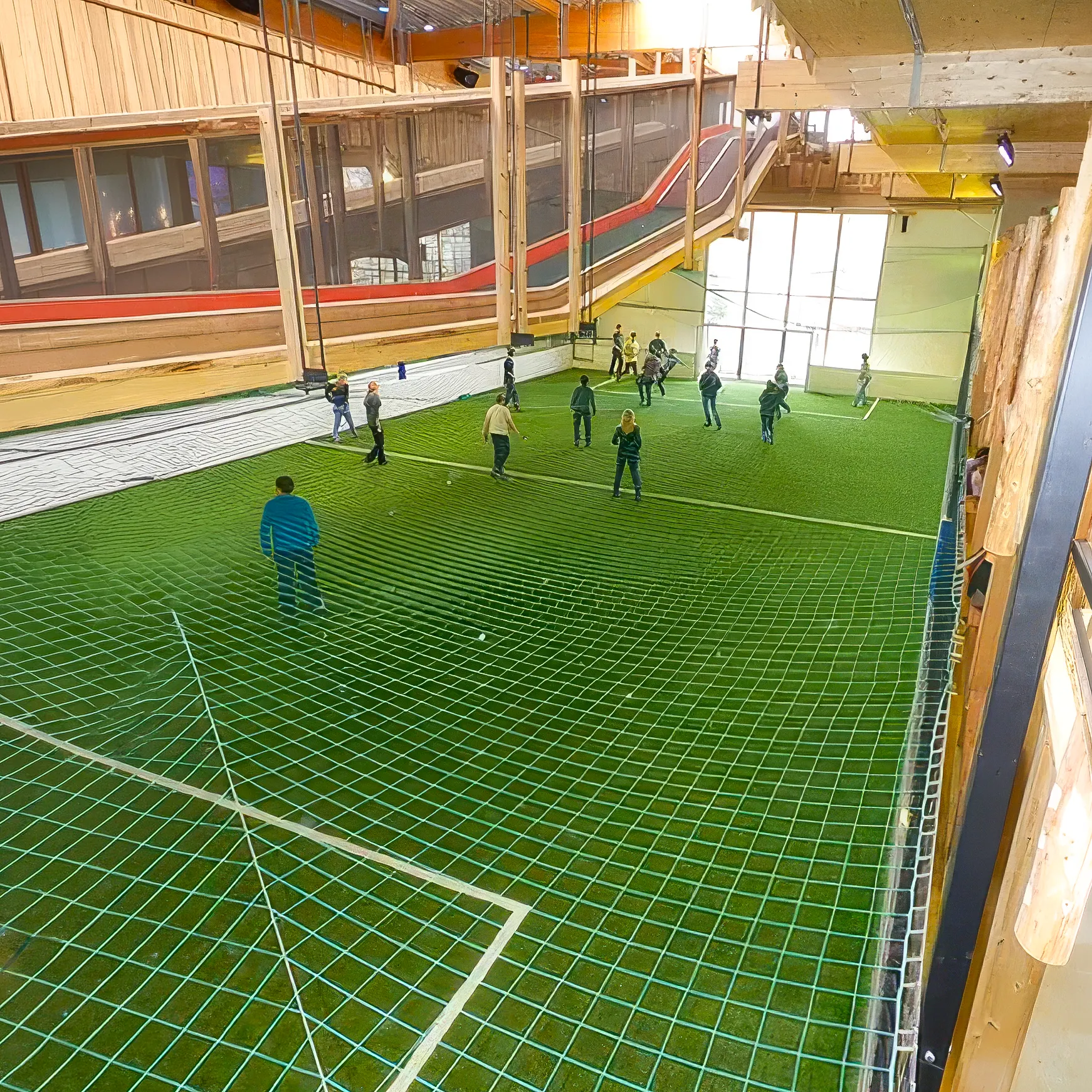 Mehrere Personen spielen in einer überdachten Halle auf einem grünen Spielfeld mit Netz.