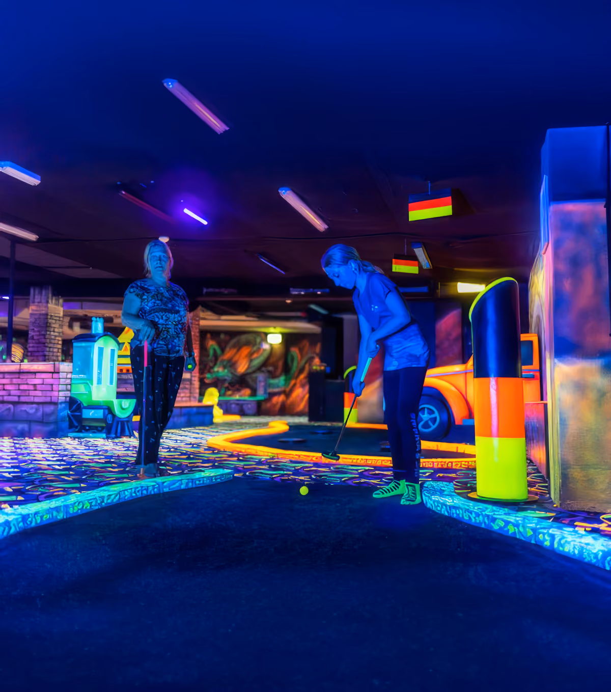 Zwei Personen spielen Minigolf in einer bunten Schwarzlicht-Minigolfhalle mit Neonfarben.