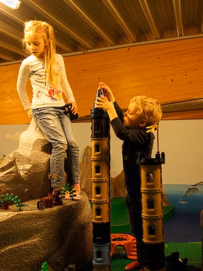Zwei Kinder spielen drinnen mit hohen Turmbauklötzen auf einem Kletterfelsen-Spielplatz.