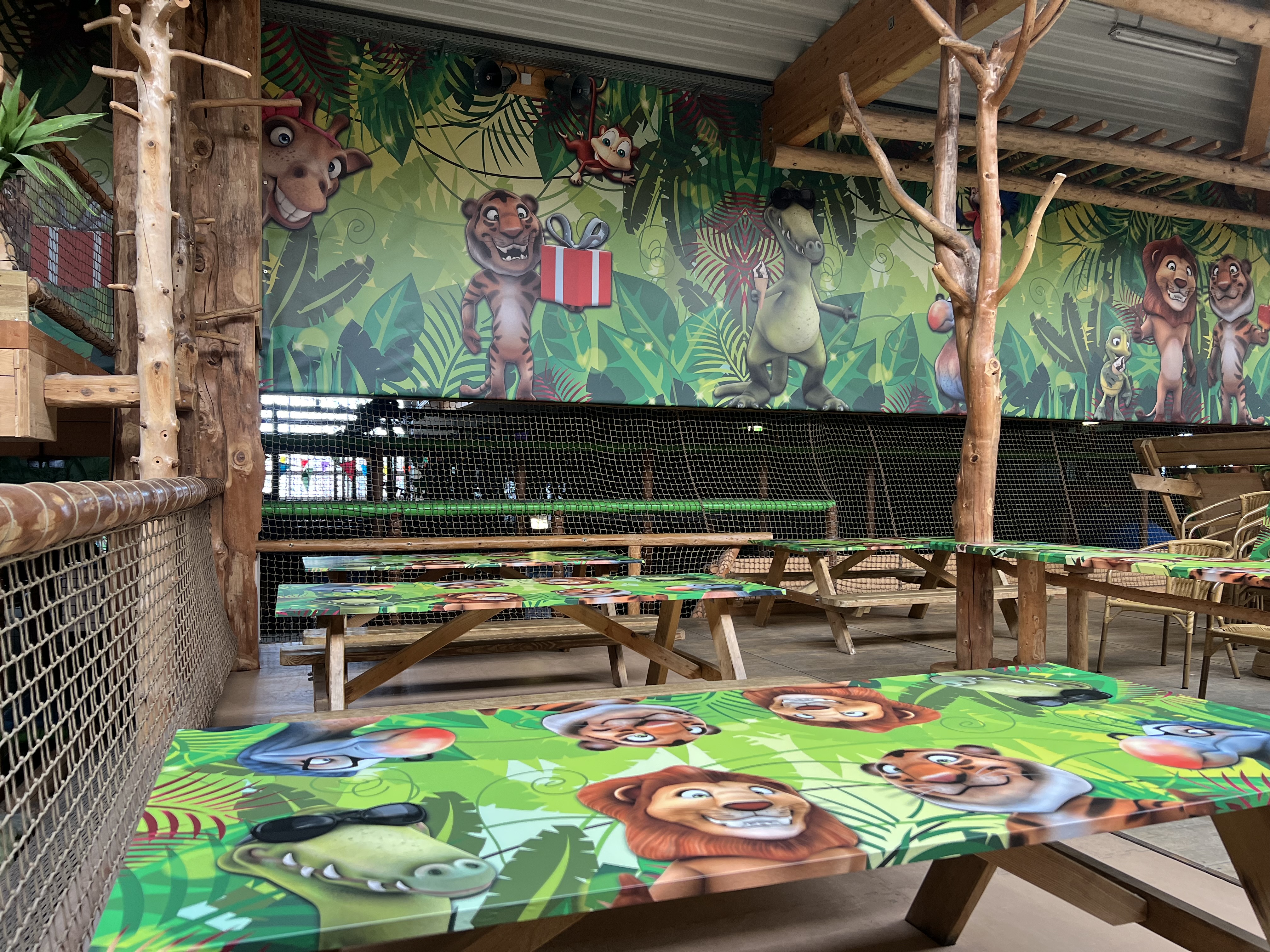 Innenbereich mit bunten Picknicktischen und einer Wand mit Cartoon-Dschungeltiermotiven.