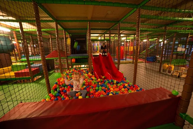 Kinder spielen in einem Innenbereich mit rot-roter Rutsche und buntem Bällebad.