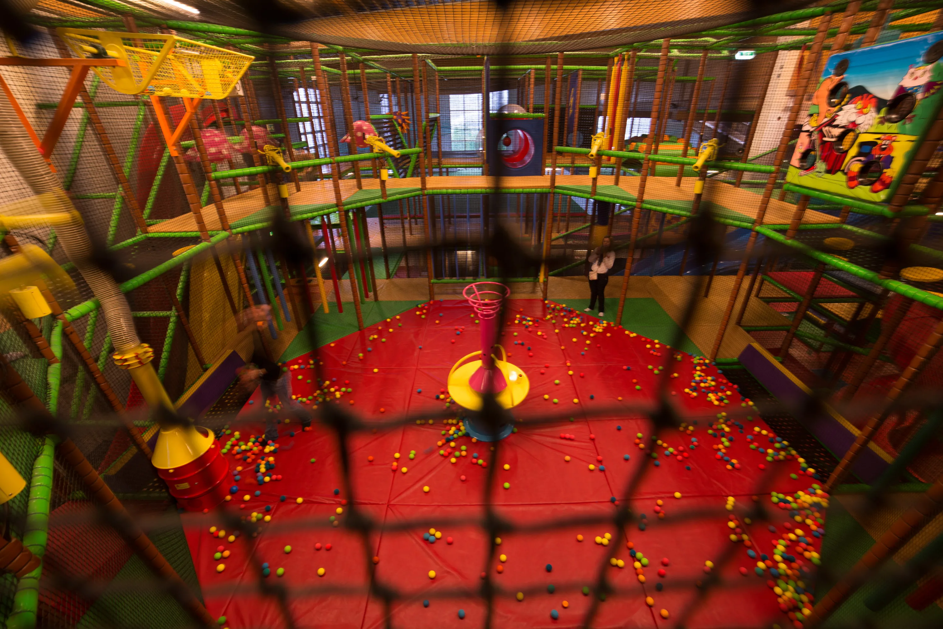 Bunte Indoor-Spielplatzarena mit roten Matten, Spielsachen und vielen kleinen bunten Bällen.
