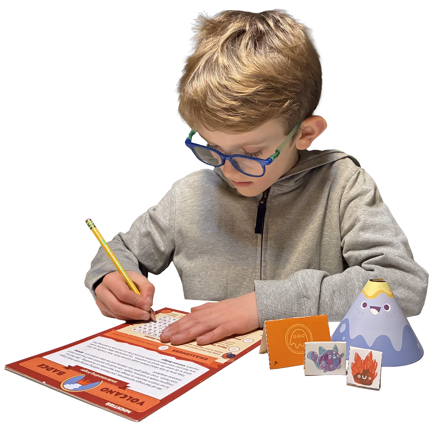Young boy wearing glasses and gray sweatshirt writing with pencil on an activity sheet with game pieces.