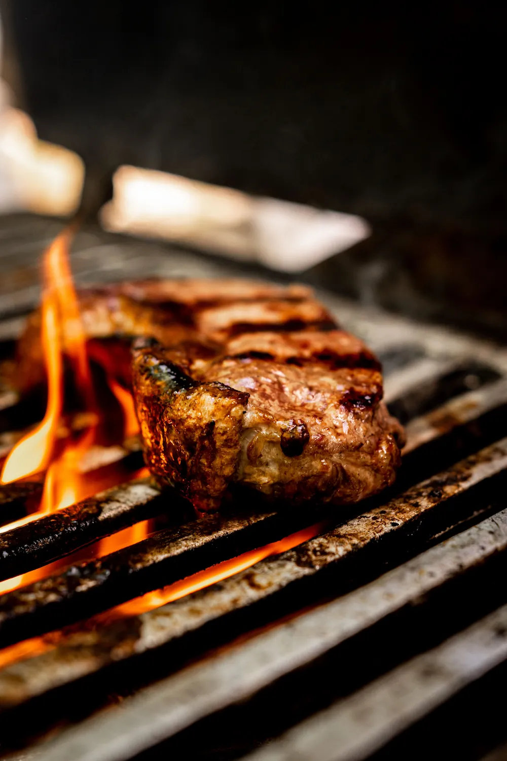 A steak searing over an open flame on a grill grate.