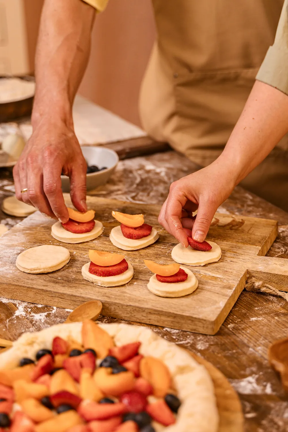 Two people's hands placing fruit on small pastry rounds during a hands-on baking class.