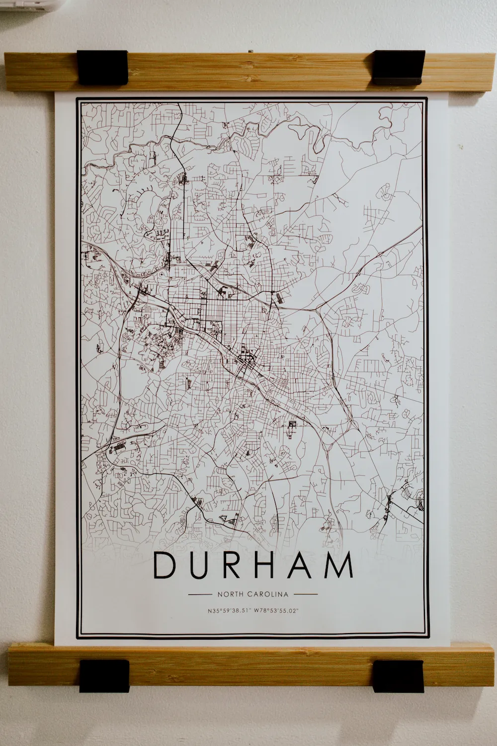 A framed black-and-white city map print of Durham, North Carolina, hanging on a wall.