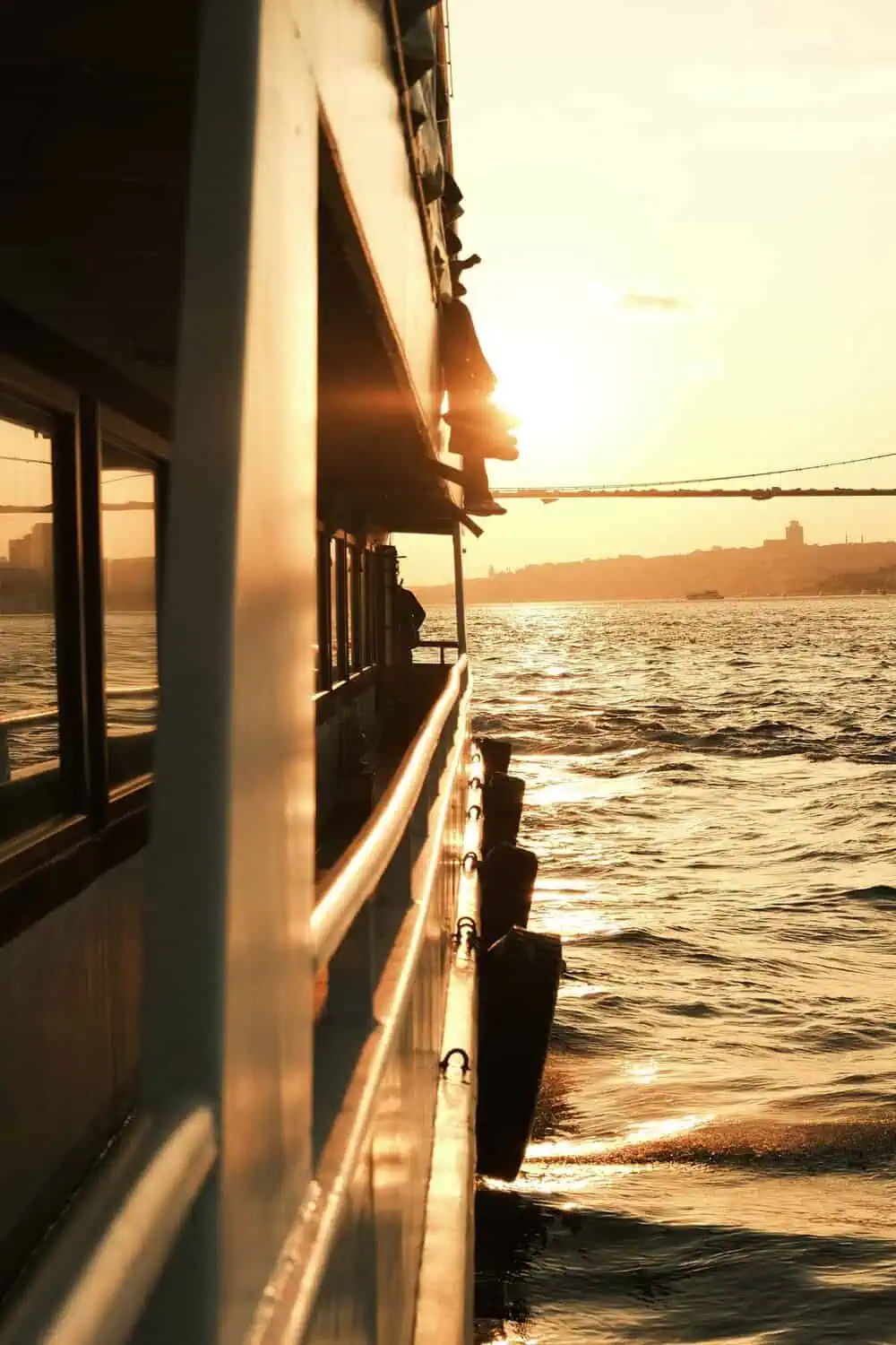 The deck of a boat at sunset, with the sun low over the water and a distant shoreline.