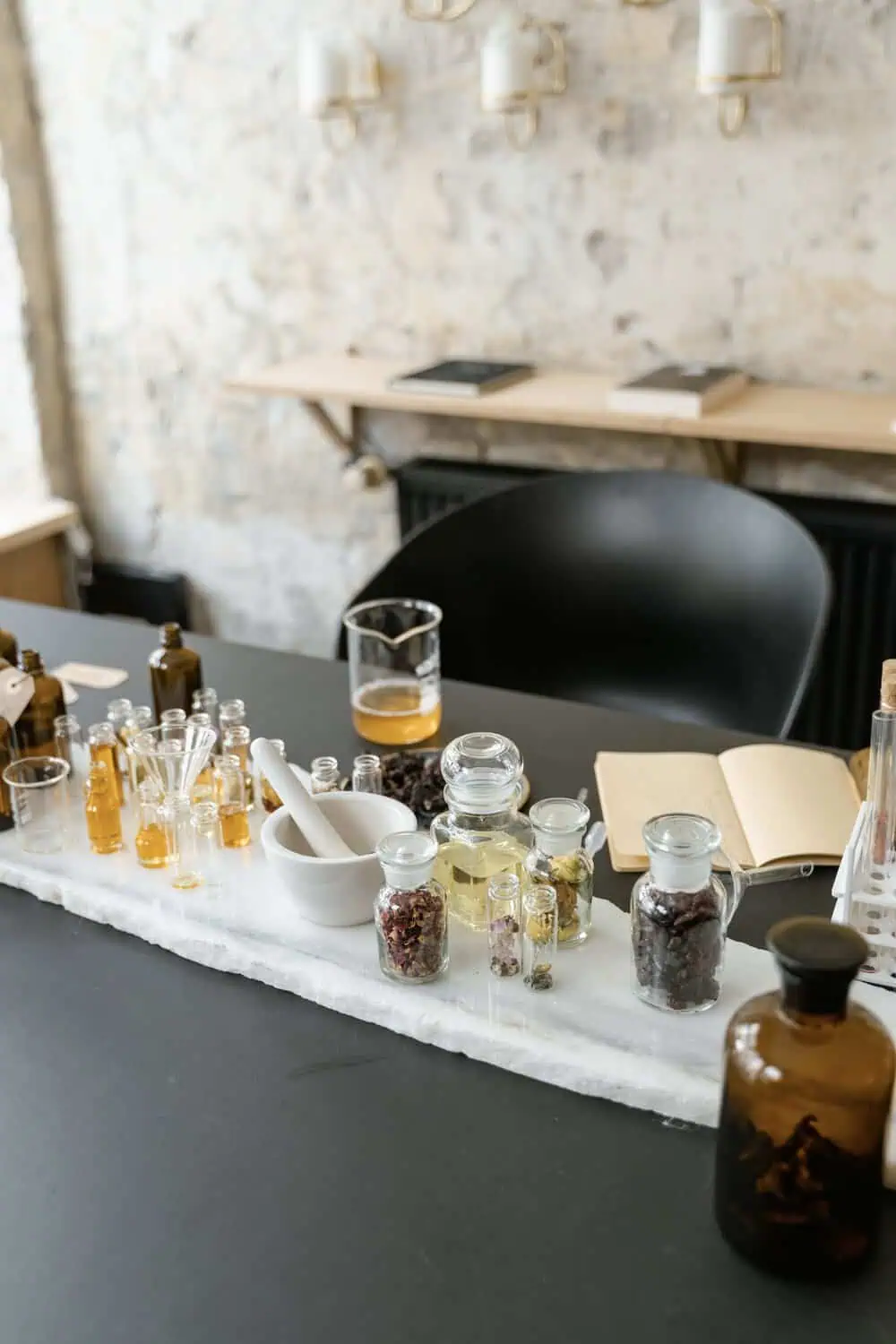 A workbench set with amber glass bottles, vials of oils, dried botanicals, and a mortar and pestle for blending perfume.