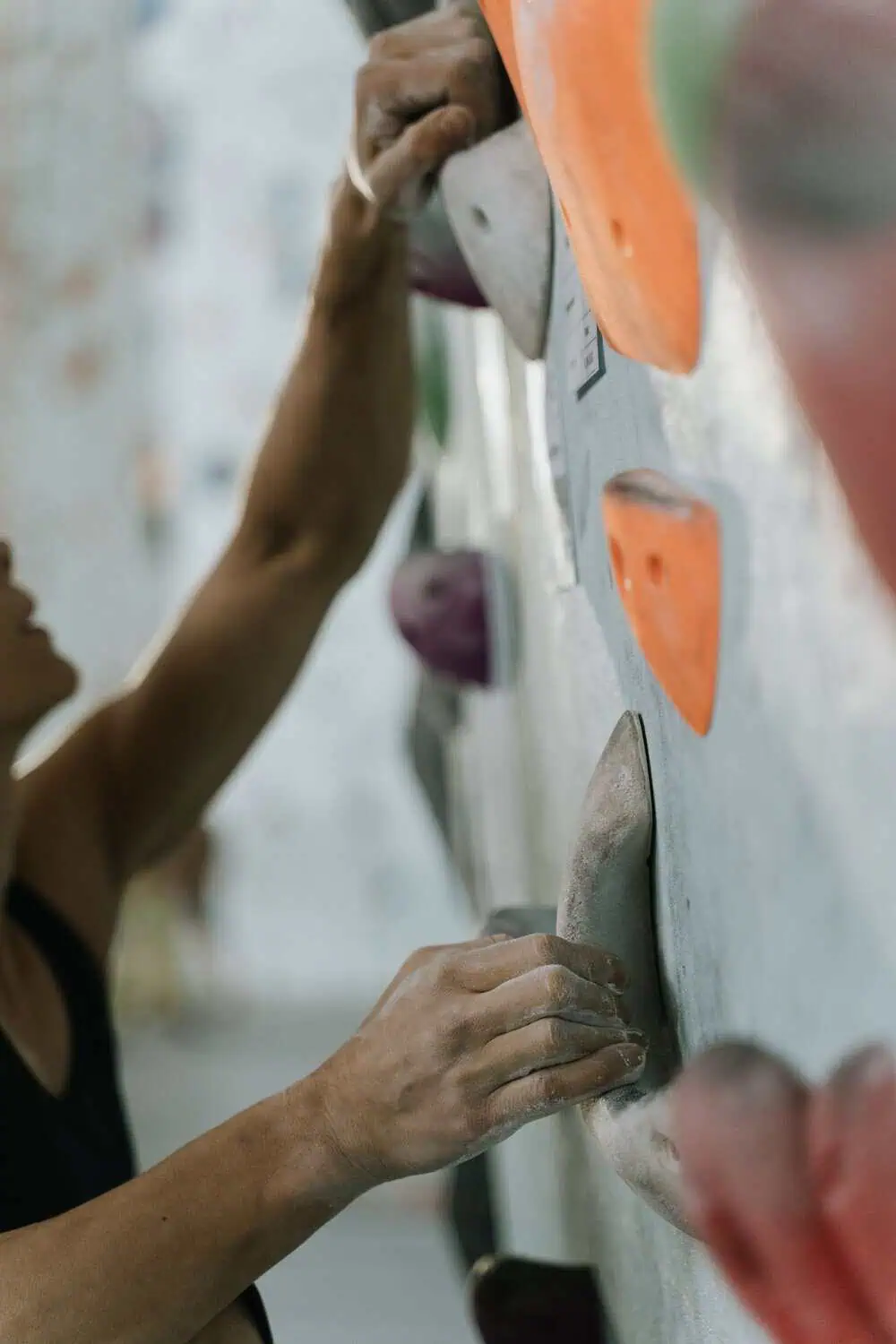 A climber's chalked hands reaching for holds on an indoor climbing wall.