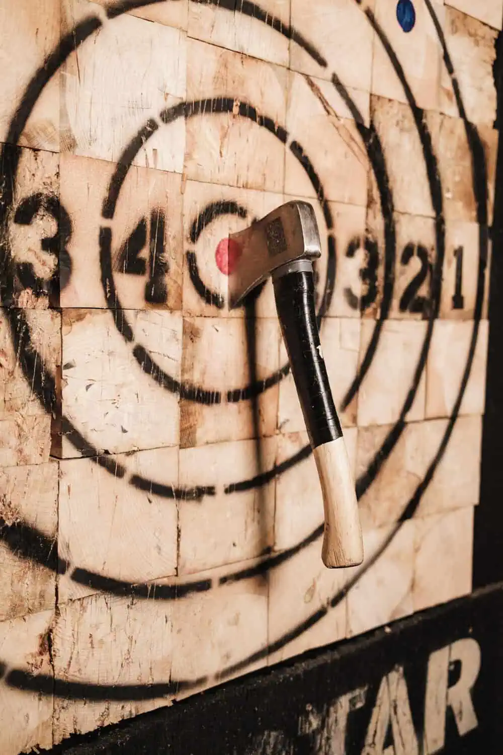 An axe lodged in the bullseye of a wooden axe-throwing target marked with scoring rings.