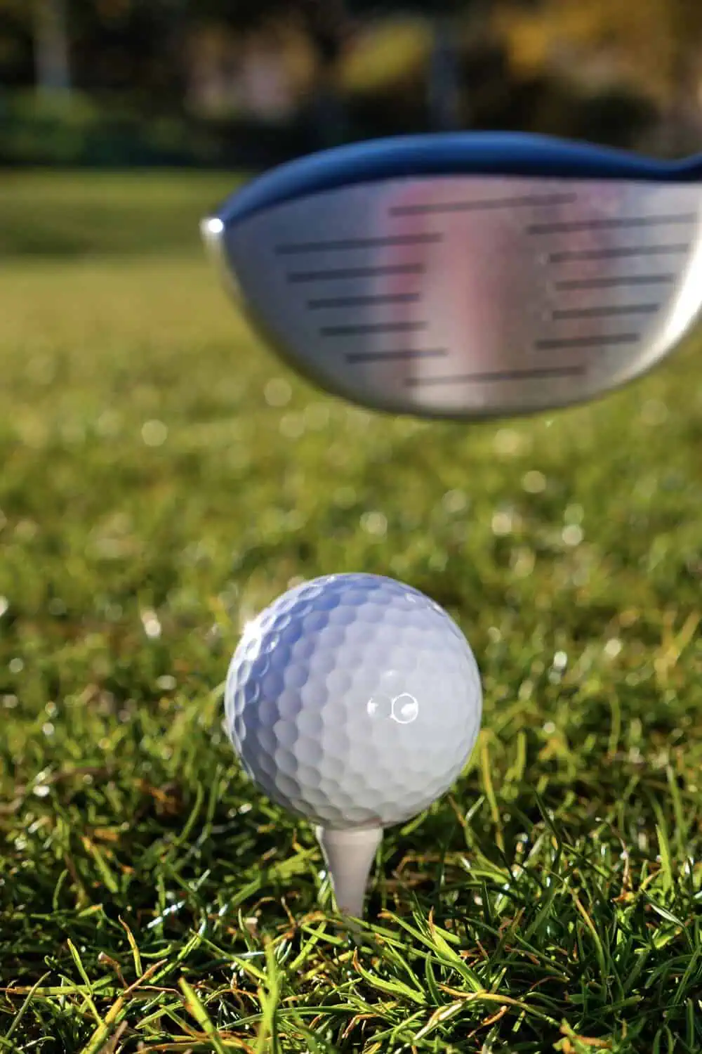 A golf club head hovering just above a teed-up golf ball on a grassy course.