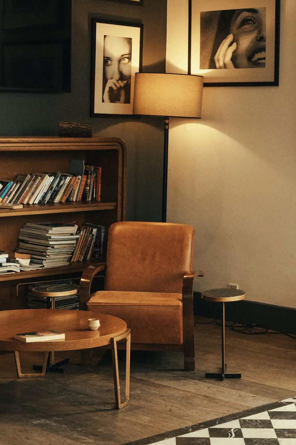 A leather armchair beside a lit floor lamp and a bookshelf in a warm, dimly lit reading corner.