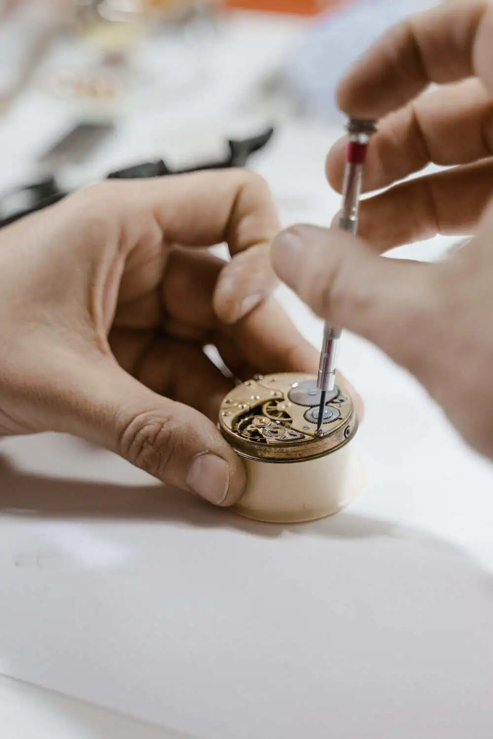 A watchmaker adjusting the movement of an open pocket watch case with fine tools.