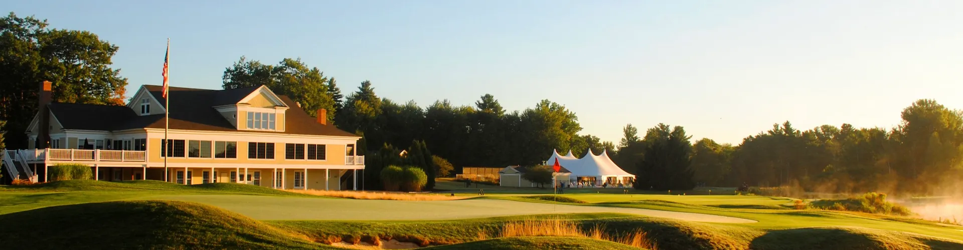 A golf course clubhouse and putting green at sunrise, with a white event tent set up nearby.