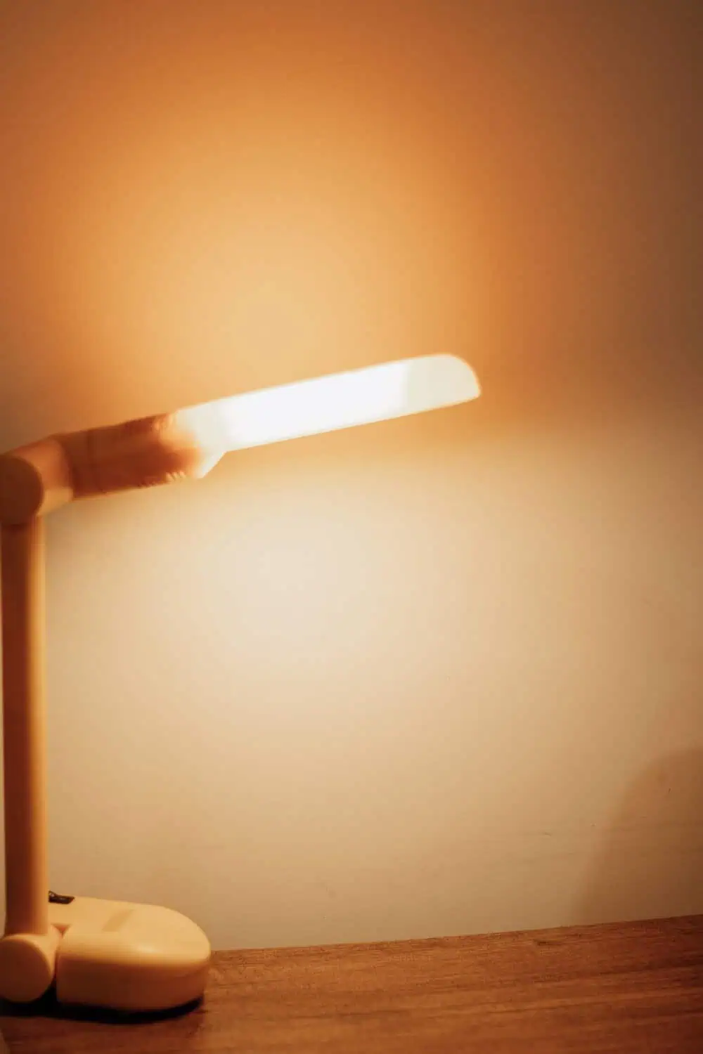 A small amber night light clipped in place, casting a warm glow across a wall in a dim room.