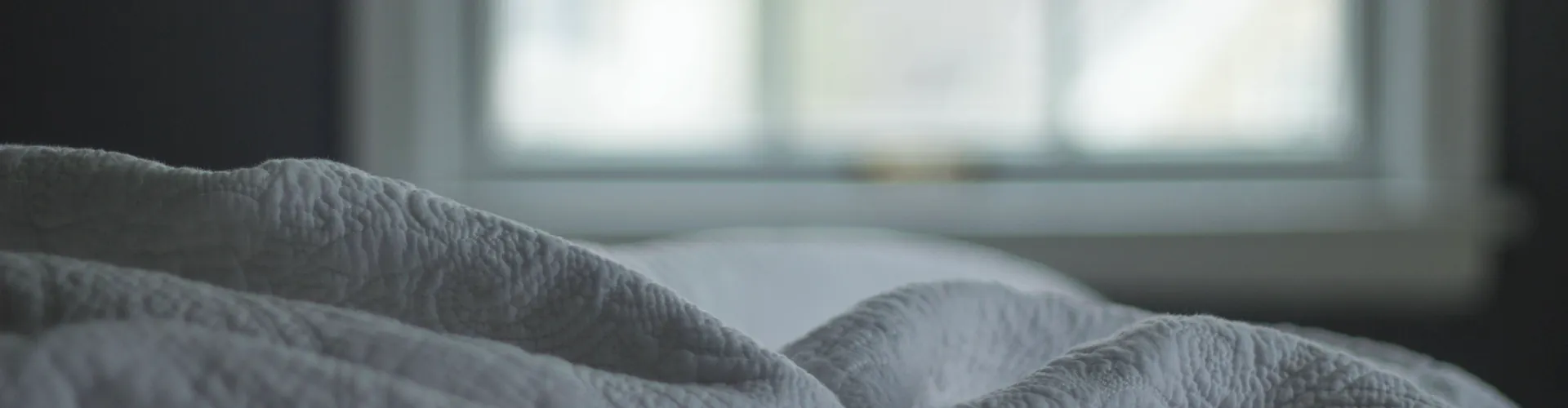 Soft folds of white quilted bedding lit by daylight from a nearby window.