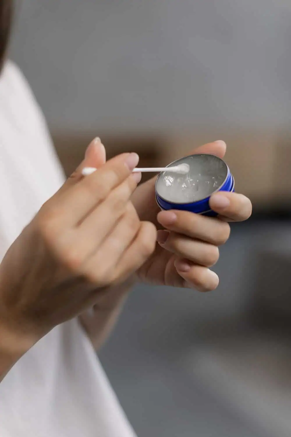 A close-up of hands using a cotton swab to apply balm from a small round tin.
