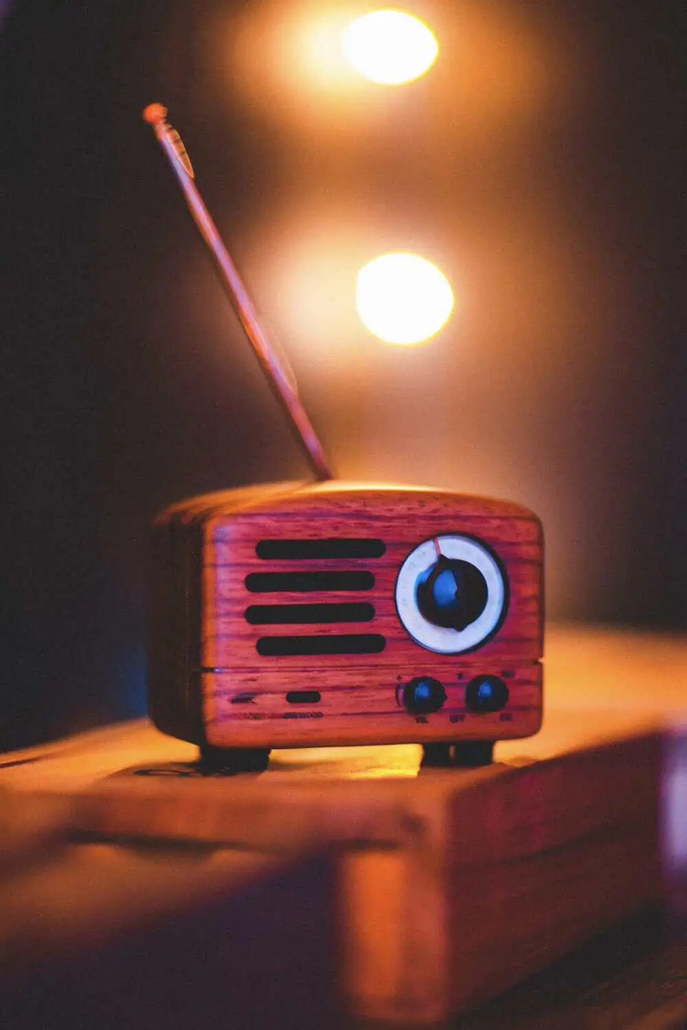 A small vintage-style wooden radio speaker with an antenna, glowing warmly beside soft bokeh lights.