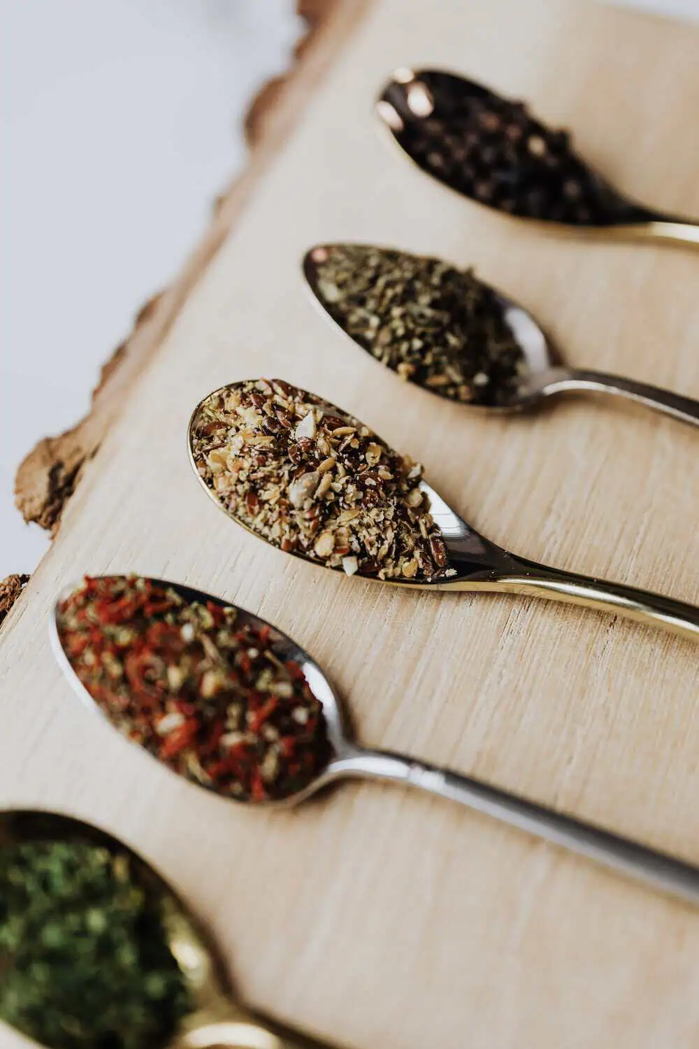 A row of spoons holding different spice blends arranged on a wood board.