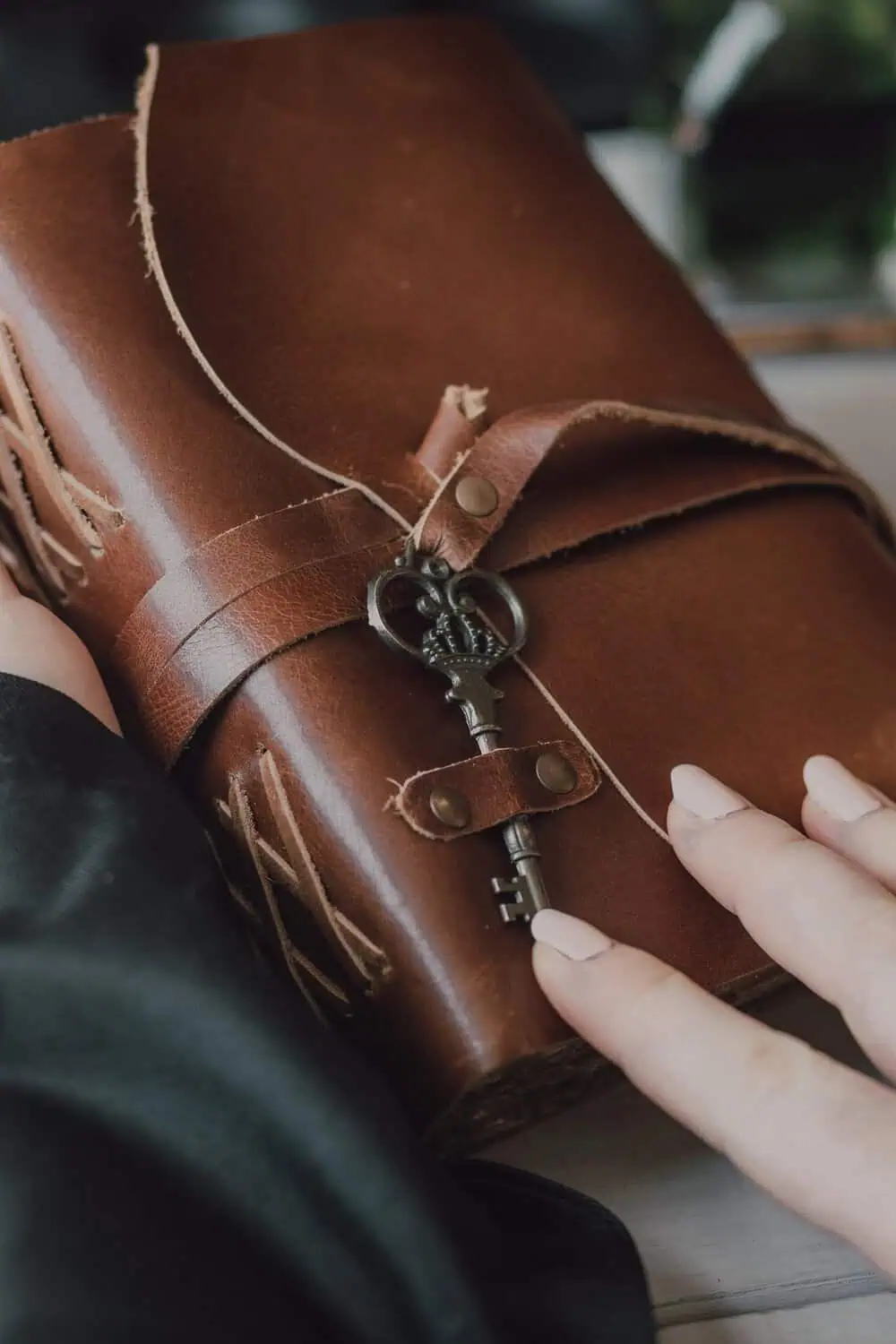 A hand resting on a leather-bound journal fastened with a vintage skeleton key.