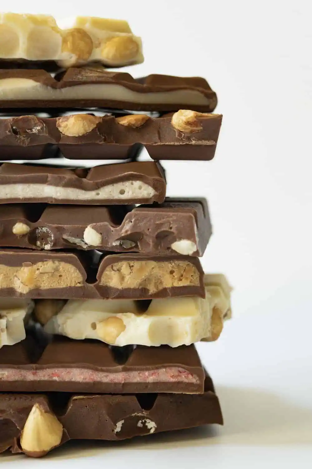 A close-up stack of chocolate bar pieces with different fillings, including hazelnuts, wafer, and fruit.