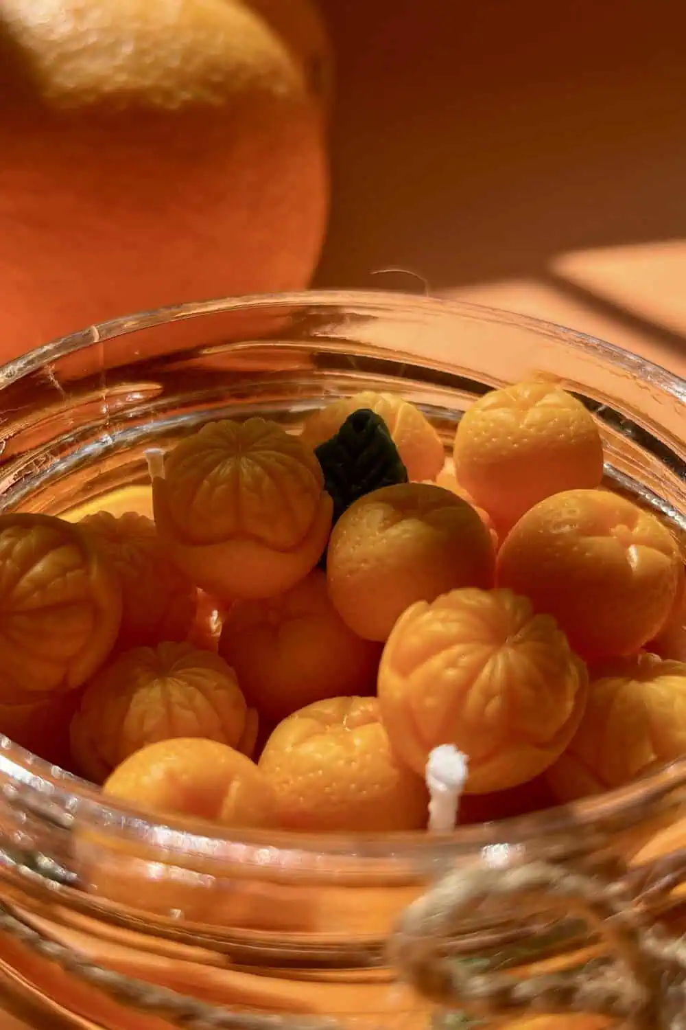 A glass jar filled with small tangerine-shaped wax candles, their white wicks visible among the fruit shapes.
