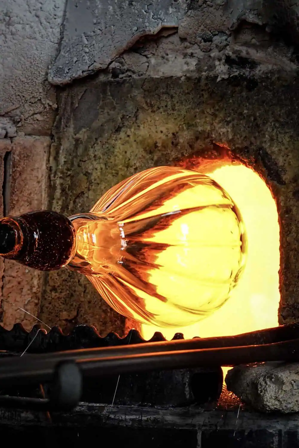 A glassblower shaping a glowing piece of molten glass pulled from the furnace.