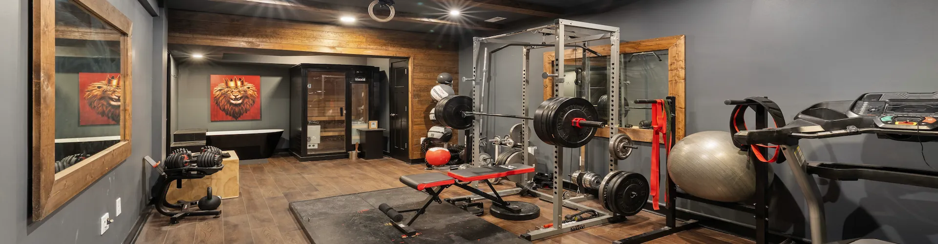A home gym corner with a power rack, weight plates, adjustable bench, and a sauna cabinet in the background.