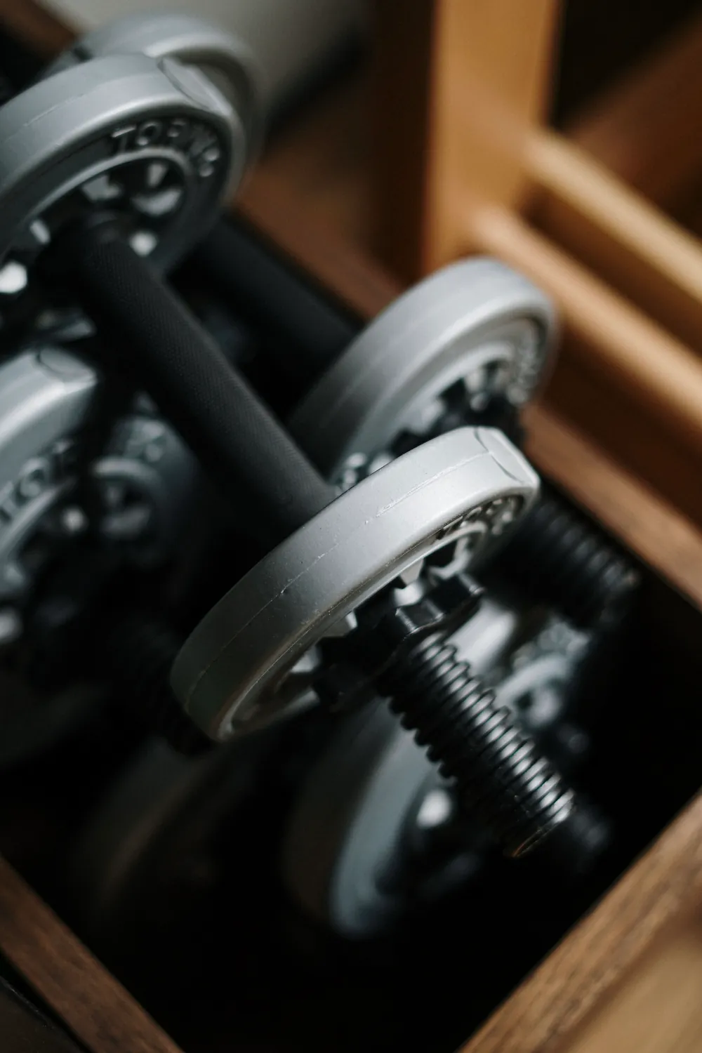 A close-up of adjustable dumbbell weight plates stacked on a barbell, resting in a wooden crate.