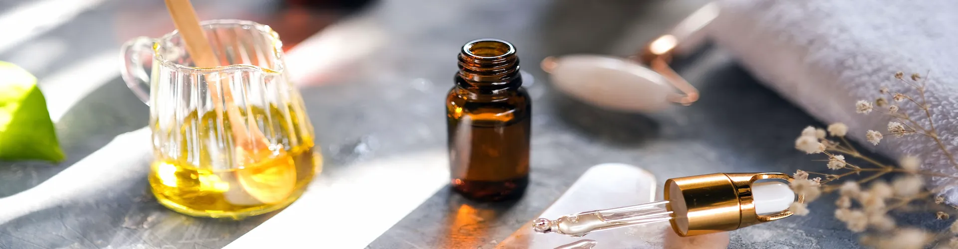 A tray of massage oils, an amber dropper bottle, a rose quartz gua sha tool, and a folded towel.