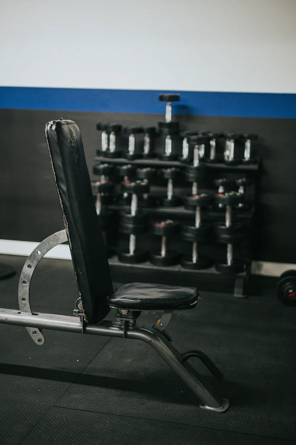 A black adjustable weight bench in a home gym with a dumbbell rack in the background.
