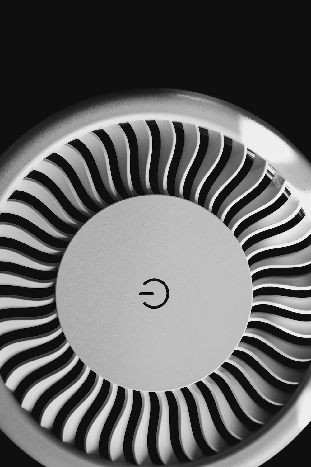 A close-up black and white photo of a round white noise machine with a power button at its center and a fan-shaped grille.