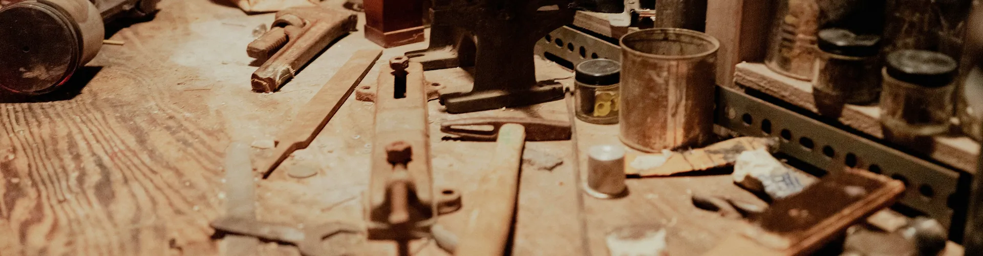 A cluttered workbench holds a vise, wrenches, small tins, and hand tools coated in sawdust.