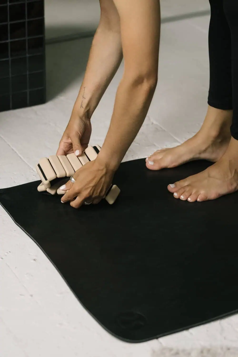 Hands adjusting the weighted blocks of an ankle weight cuff on a yoga mat, barefoot.