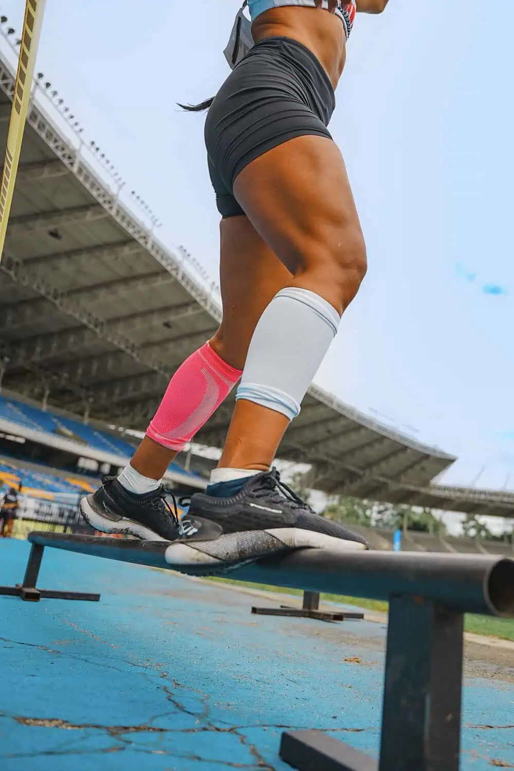 A runner's legs wearing pink and white compression calf sleeves on an outdoor track.