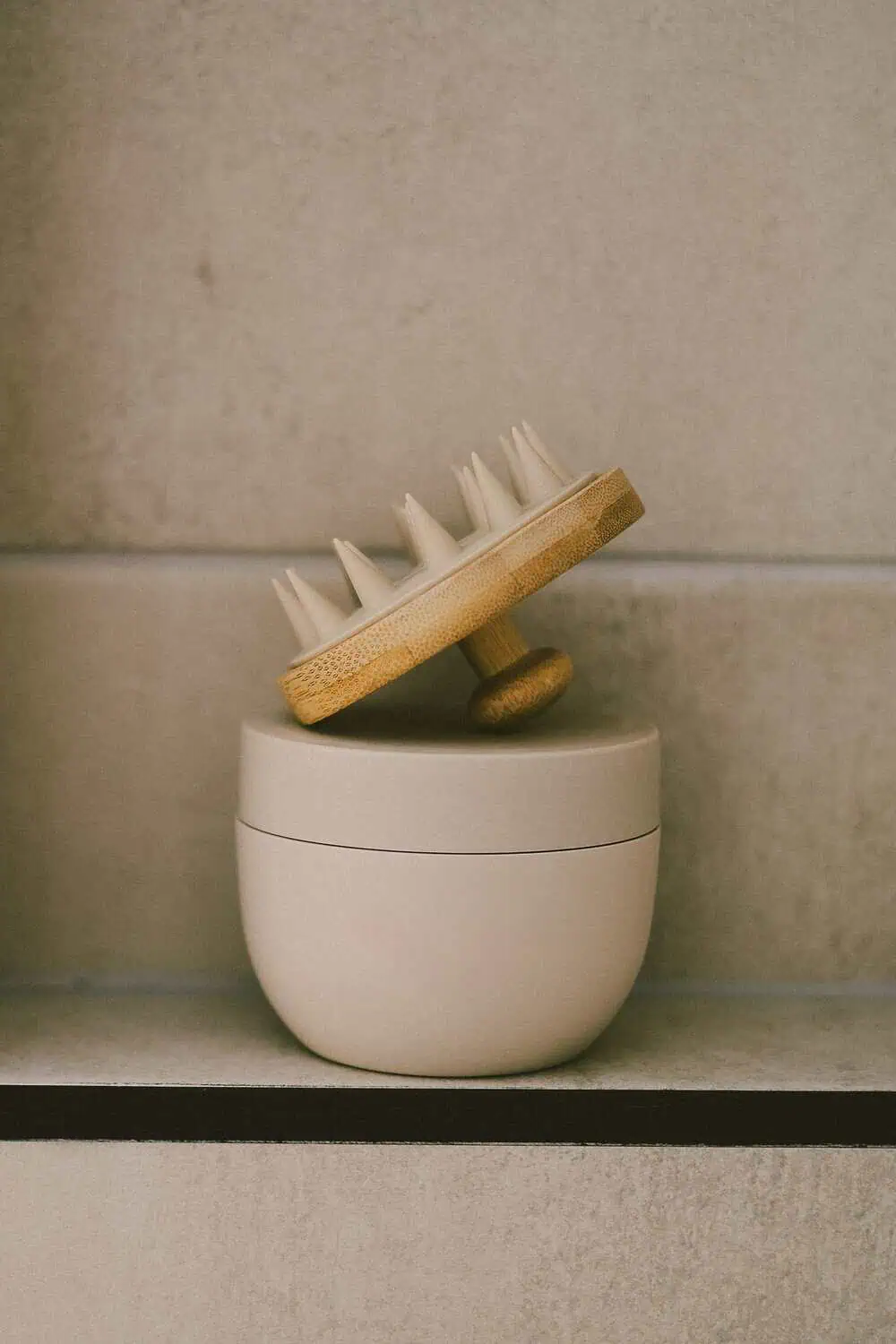 A bamboo-handled scalp massager resting on top of a ceramic jar.