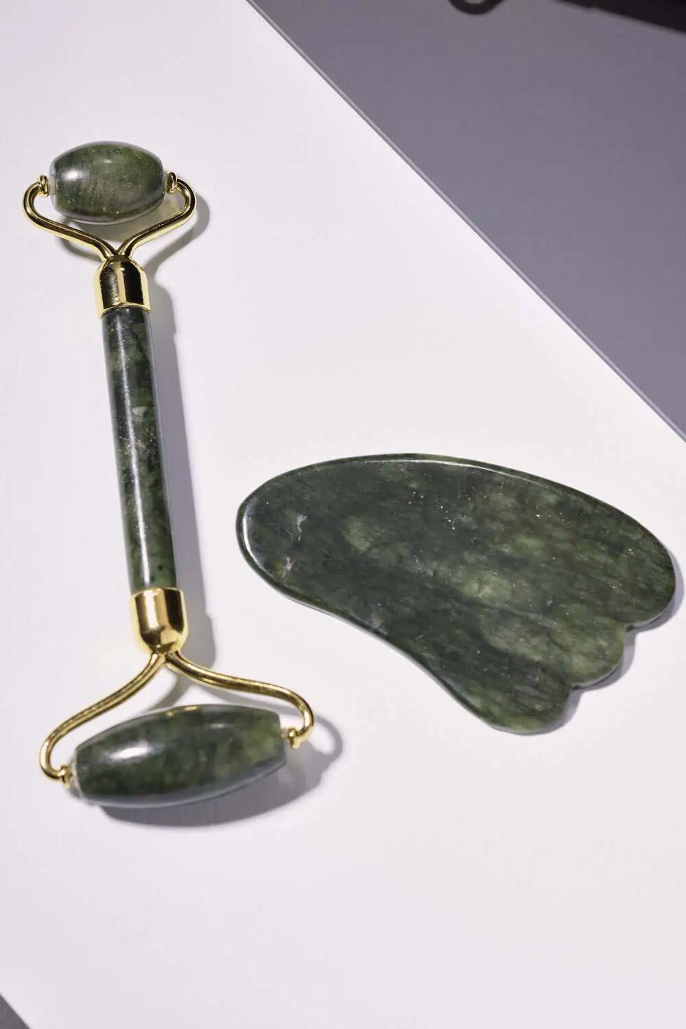 A jade roller and a gua sha stone with gold accents laid on a light surface.