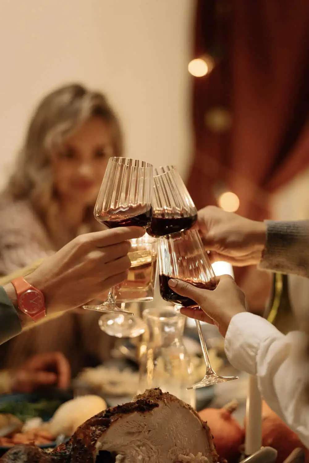 Hands clinking wine glasses over a decorated holiday dinner table.