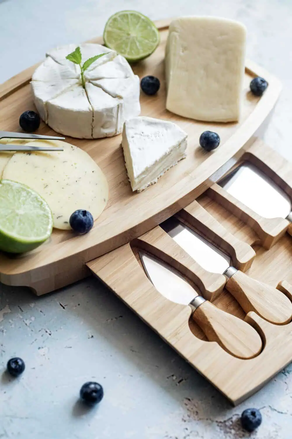 A cheese board with a knife set, assorted cheeses, blueberries, and lime.