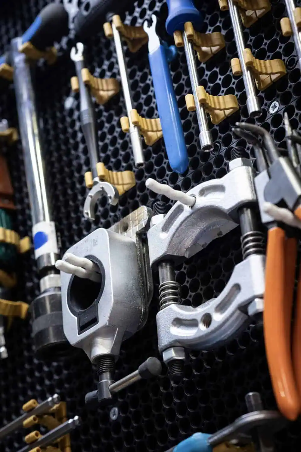 A pegboard wall holds an organized array of wrenches, screwdrivers, clamps, and pliers on hooks.