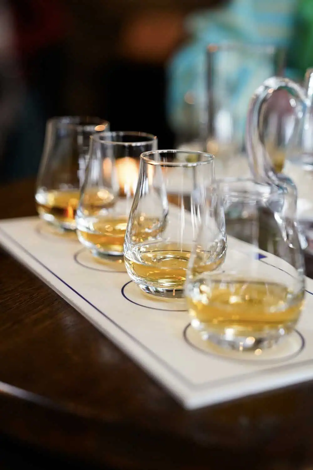 Four glasses of whiskey, each poured to a different level, are lined up on a tasting flight board.