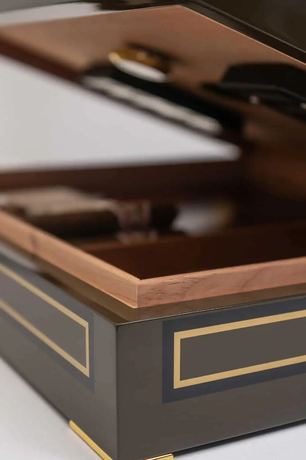 An open wood-lined humidor box with gold trim reveals a row of cigars stored inside.