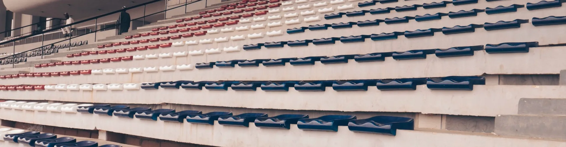 Rows of empty stadium seats in red, white, and navy blue rise toward the upper deck.