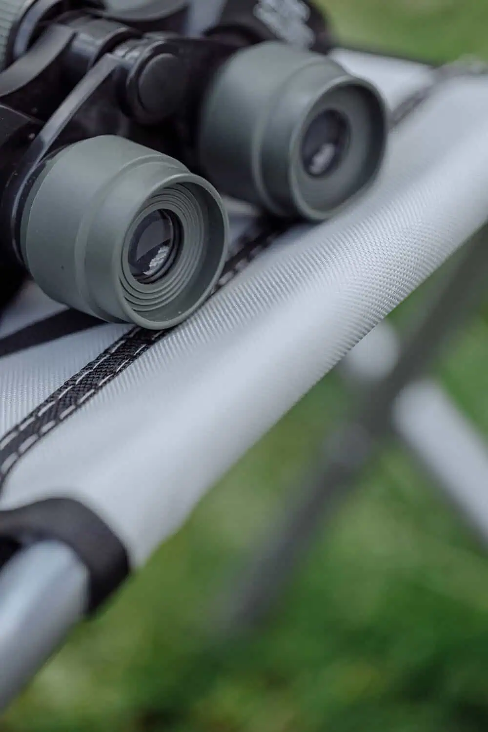 A pair of binoculars with green rubber eyecups rests on folded outdoor gear.