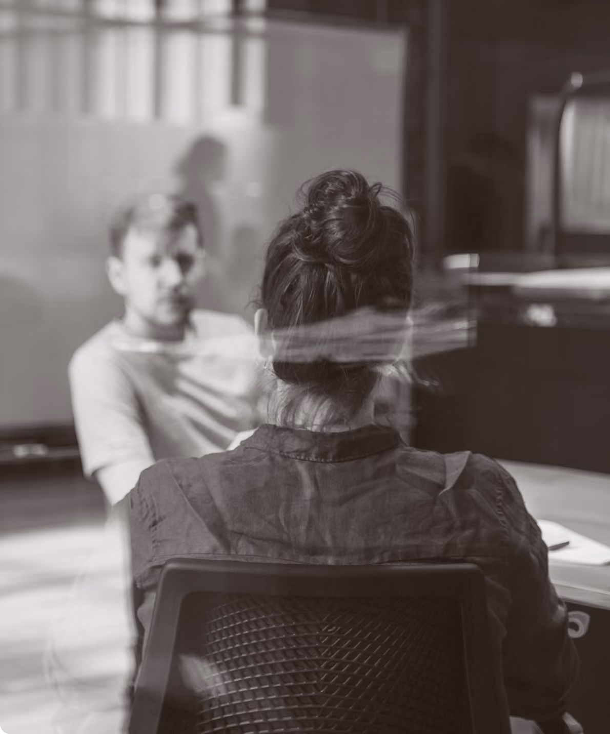 Black and white image of a man and a woman engaged in conversation in an indoor setting.