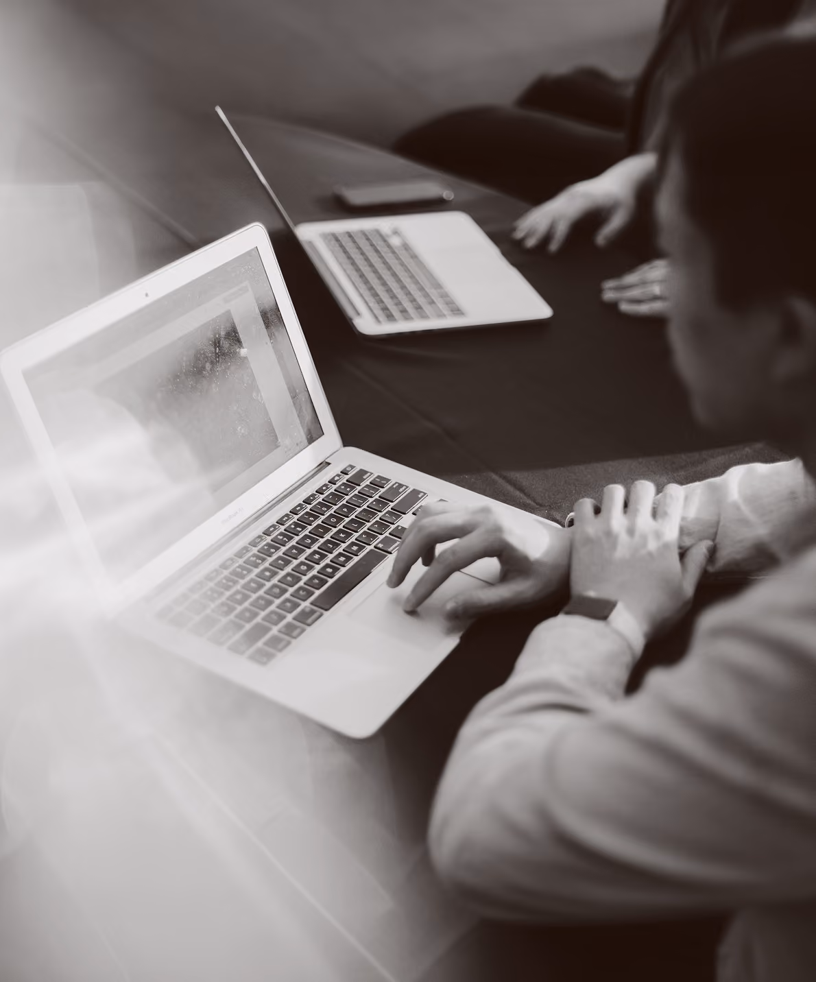 Two people sitting at a table using laptops, one person typing on a MacBook Air.