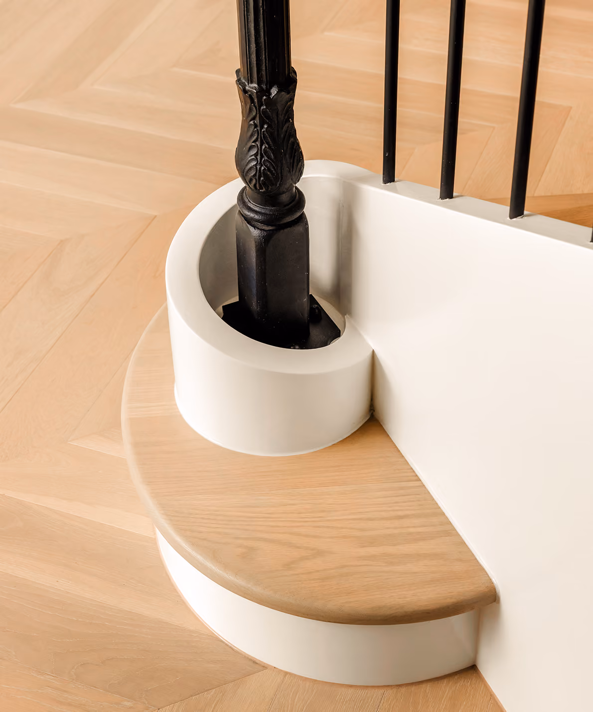 Curved wooden stair step with white base and black decorative banister post fit into circular white support.